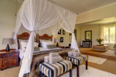 a bedroom with double bed, sheer curtains, small bench in front of it