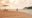 A couple spending time on a golden sandy beach at sunset looking at the ocean with a lounge chair and a red umbrella behind them