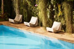 a pool area with three white lounge chairs and green wall behind it