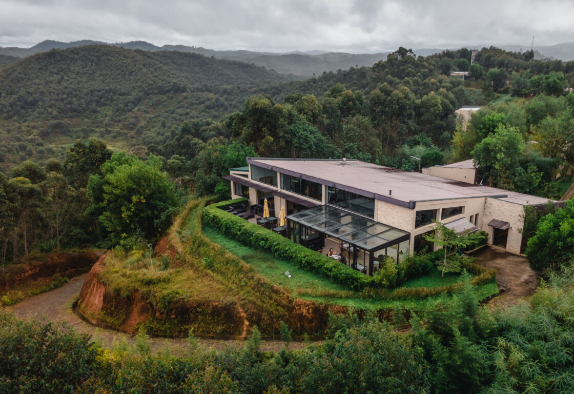 Modern rainforest lodge at Mantadia, Andasibe, set on a hillside and surrounded by lush forest and rolling green hills under a cloudy sky.