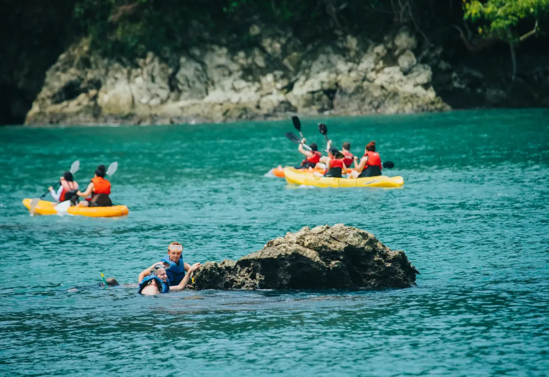 A group of people paddling in rafts on a lake, surrounded by water, wearing life jackets and enjoying outdoor recreation.