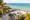 Tropical beach with thatched huts and palm trees overlooking clear turquoise ocean. Sandy shore with lounge chairs.