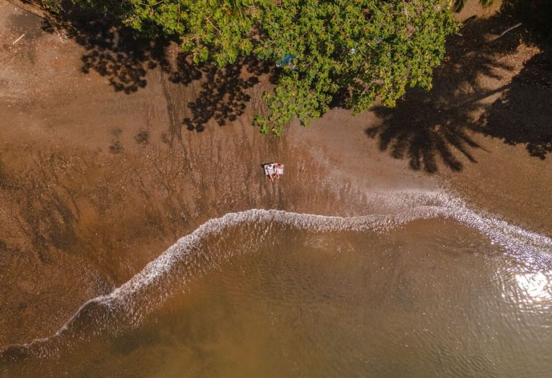 Aerial shot of a beach wit golden sands and a couple lying down close to the shore