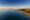 Panoramic aerial shot of the coast at sunset. Serene and calm blue water to the left, and a sandy beach fringed by green trees and houses dotted in between them, fringe the beach