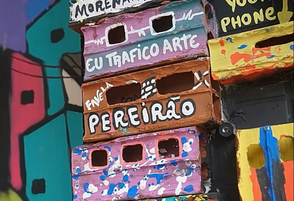 A closeup of an artwork made up of stacked bricks which are painted colourfully with painted portugese text.