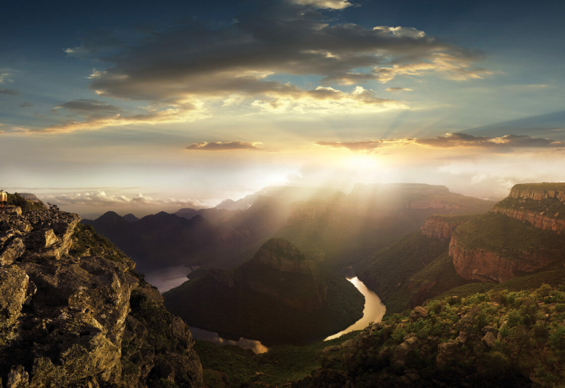 Sun breaks through clouds of aerial shot of a river running through a mountainous green valley