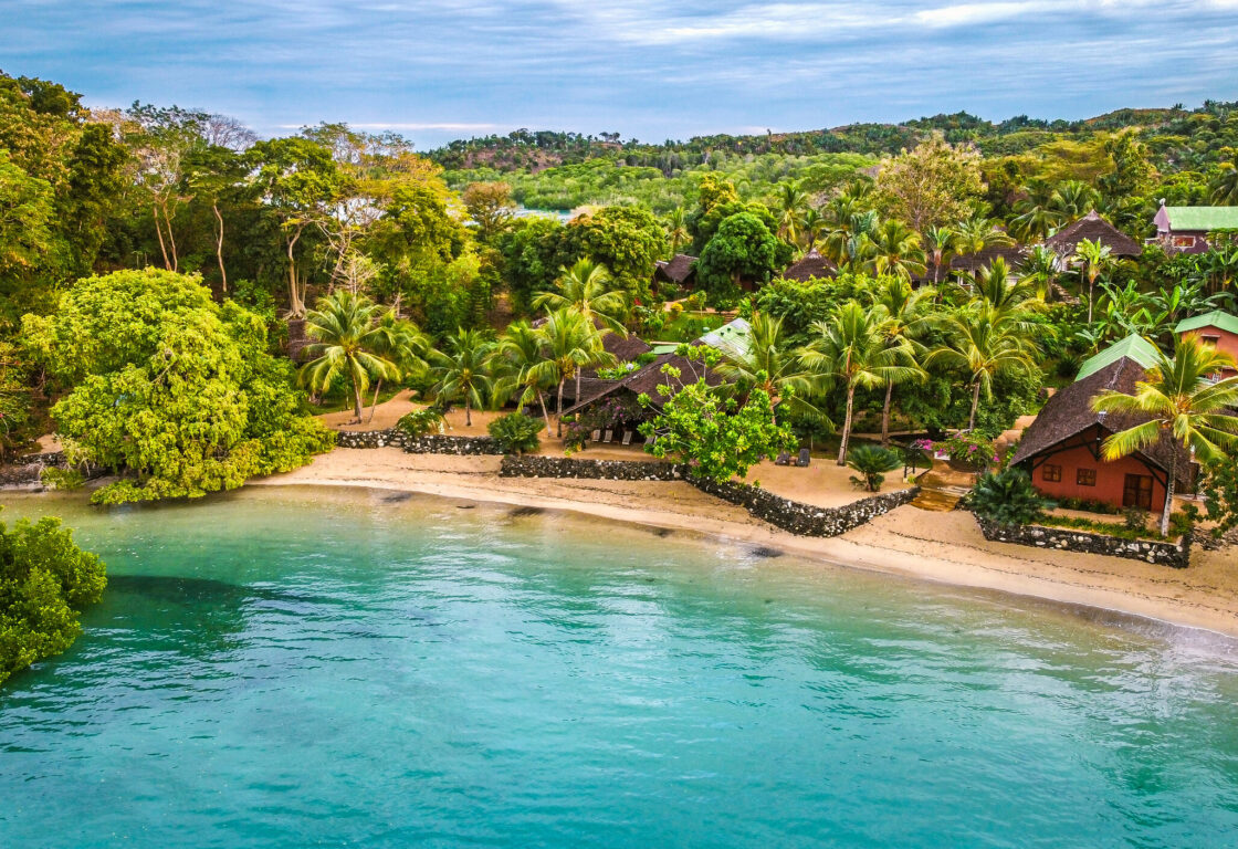 an aerial view of a lodge located in the middle of a green forest located by the beach and ocean
