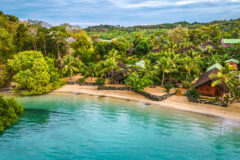 an aerial view of a lodge located in the middle of a green forest located by the beach and ocean