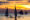 a sunset in Boracay philippines creates a golden stripe in the sky and the silhouettes of traditional fishing ships with large sails and poles to balance the boat sit on calm water and on one boat, for people sit and dangle their feet in the water