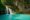 Kawasan Falls in the philippines the side of a cliff with grass and greenery growing and on the left two streams of water rush into a turquoise pool at the bottom
