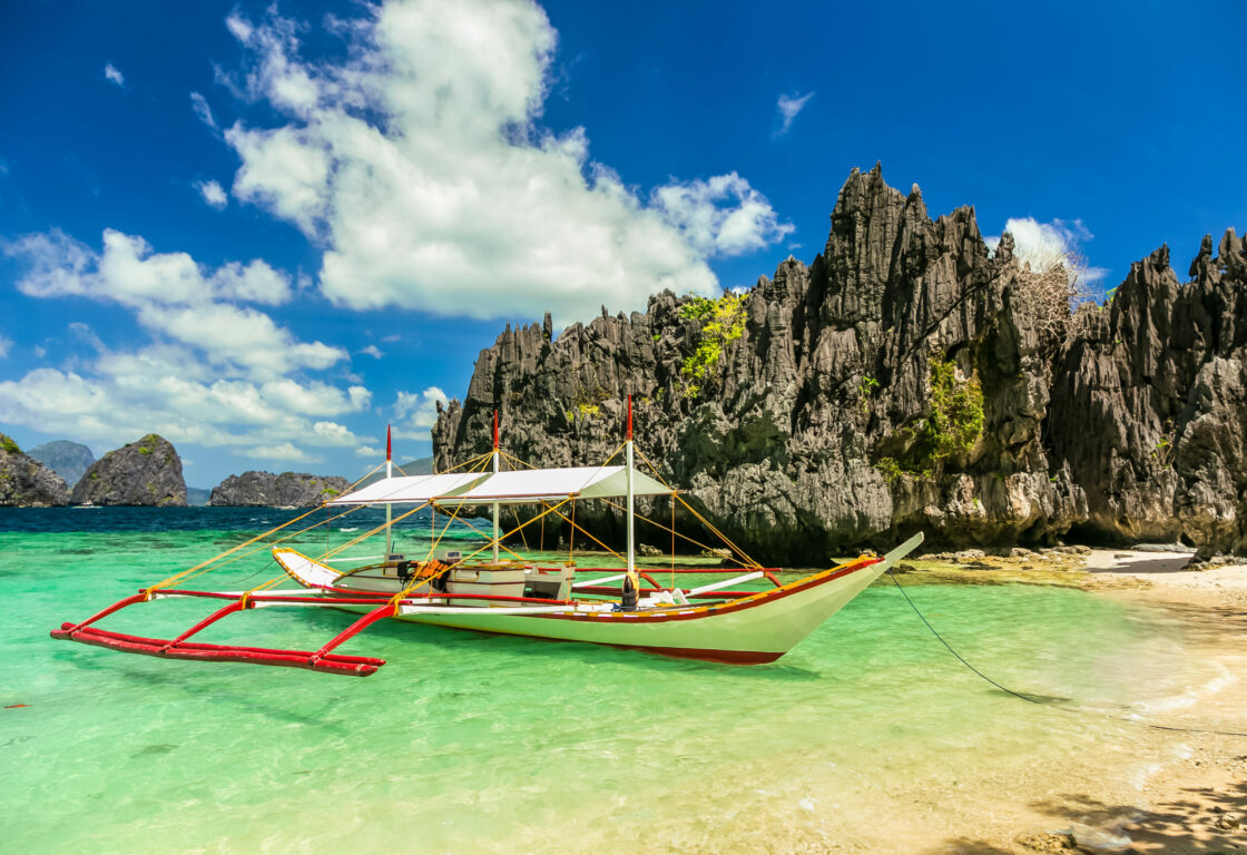 A bangka boat in the philippines a long wooden boat with poles to keep it balanced sits on crystal clear sea and limestone cliffs rise from around it