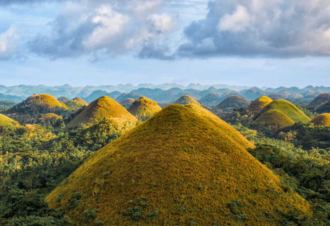 symmetrical, grass-covered mounds stretching across the landscape some with pointed tips and some rounded, at the chocolate hills in bohol in the philippines