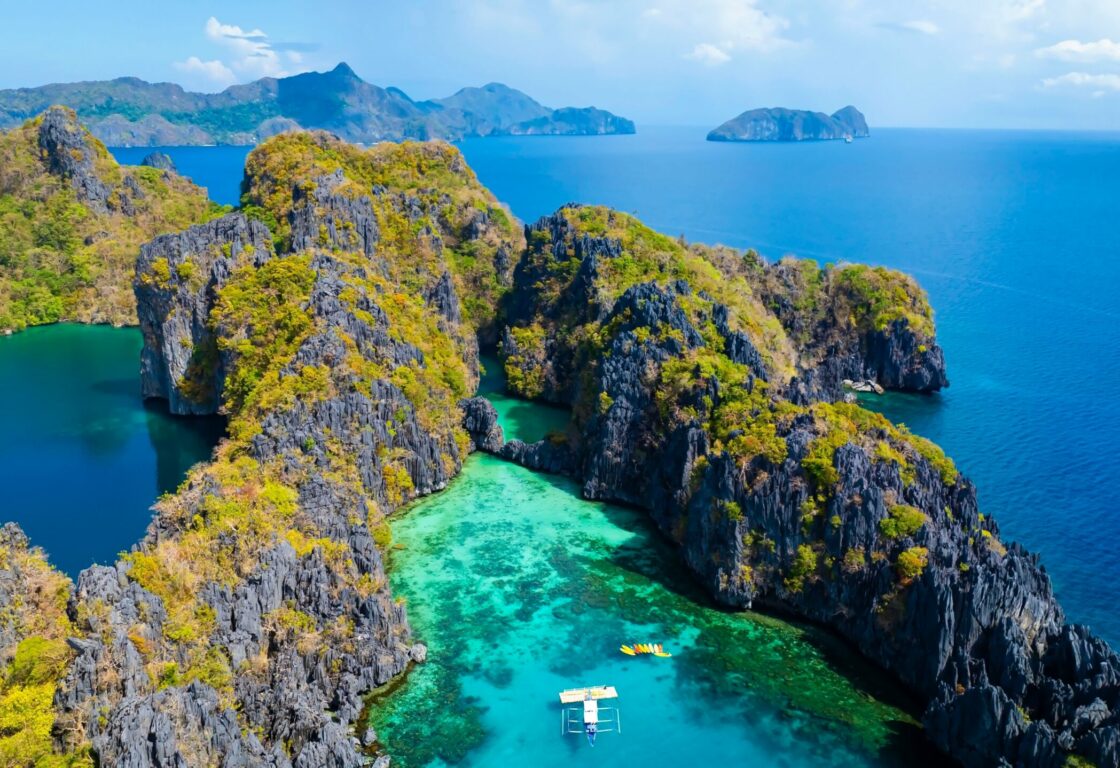 aerial view of the small lagoon in el nido where limestone cliffs create a cove separate from the rest of the sea and boat with kayaks waits in the middle of the water