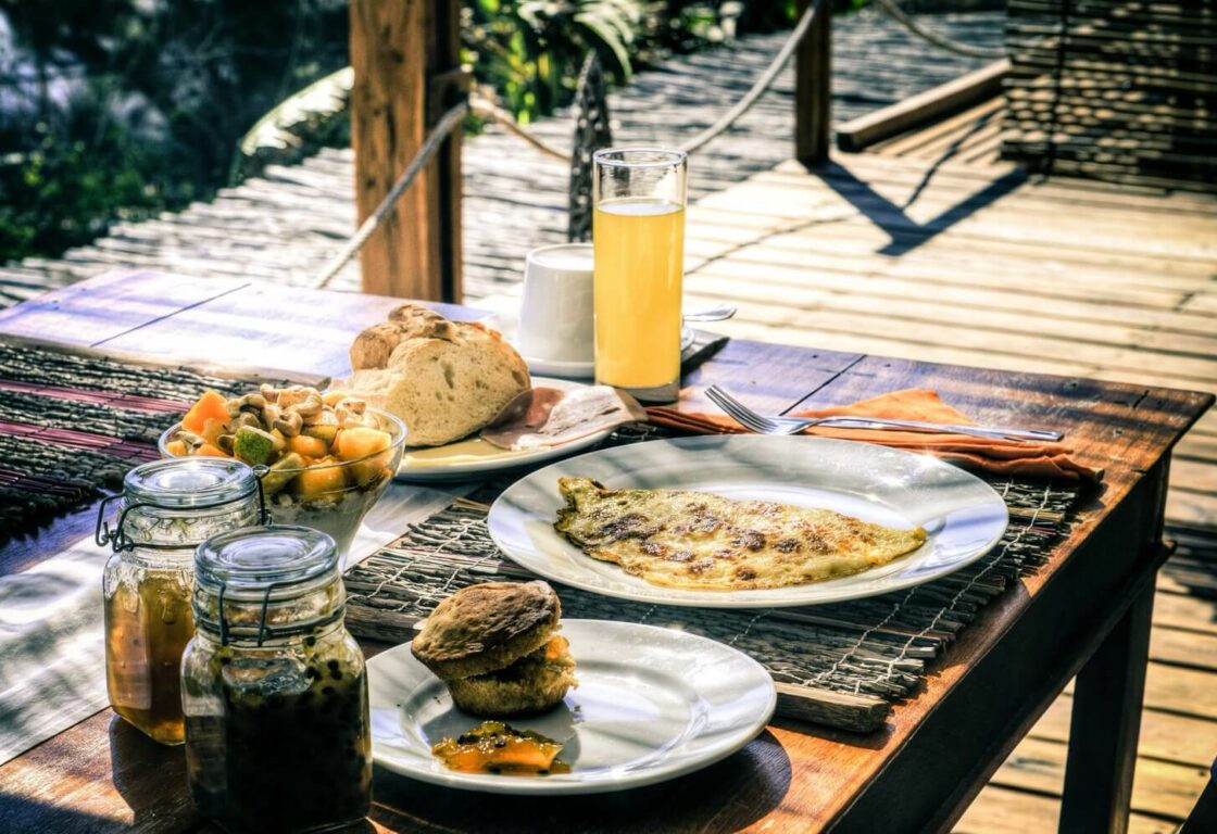 A table with plates of food including pancakes, eggs, pastries and a glass of orange juice