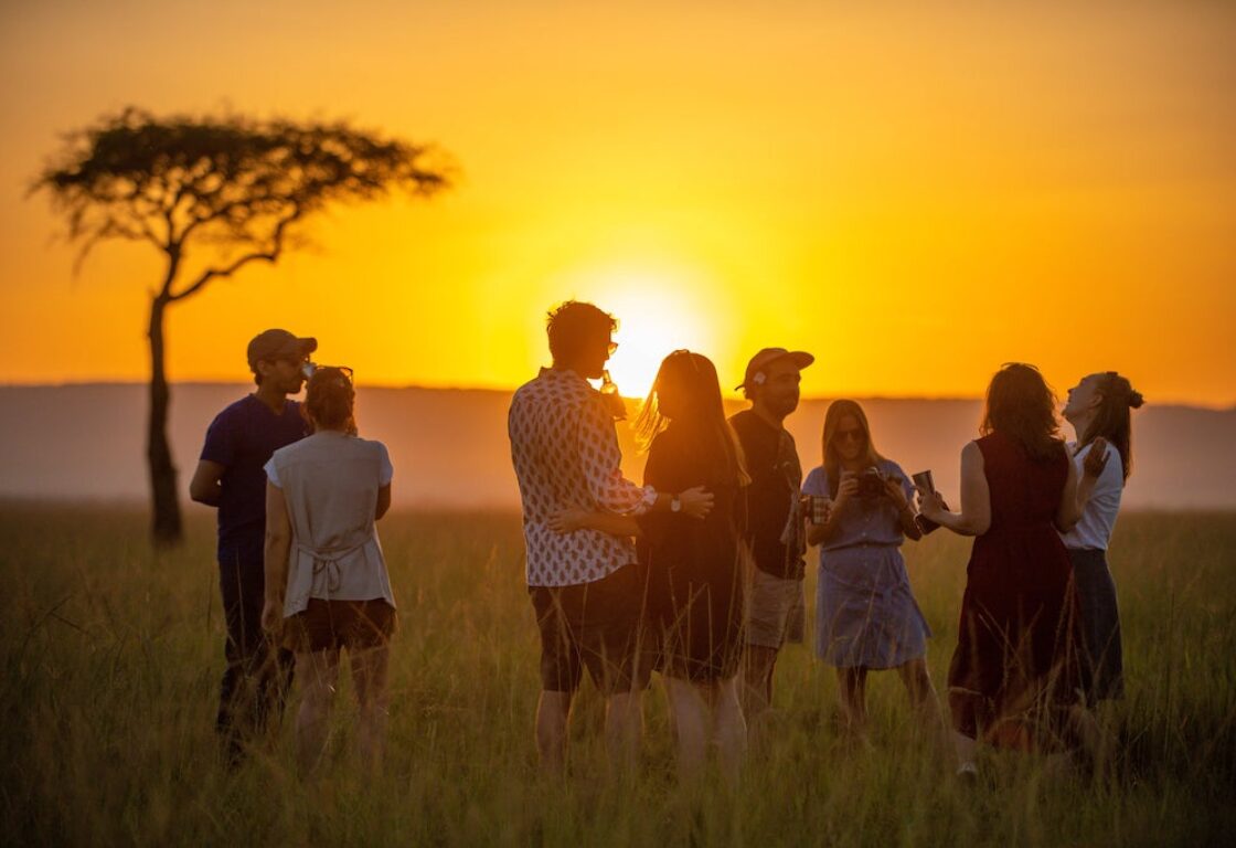 A group of around 10 people stand around enjoying a sunset in front of an African Savannah