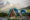 several green domes are located within Patagonian nature surrounded by mountains and trees and rainbow above it