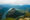 Aerial view of lush green canyon with a winding river, surrounded by rugged mountains beneath a cloudy sky, evoking tranquility and grandeur.