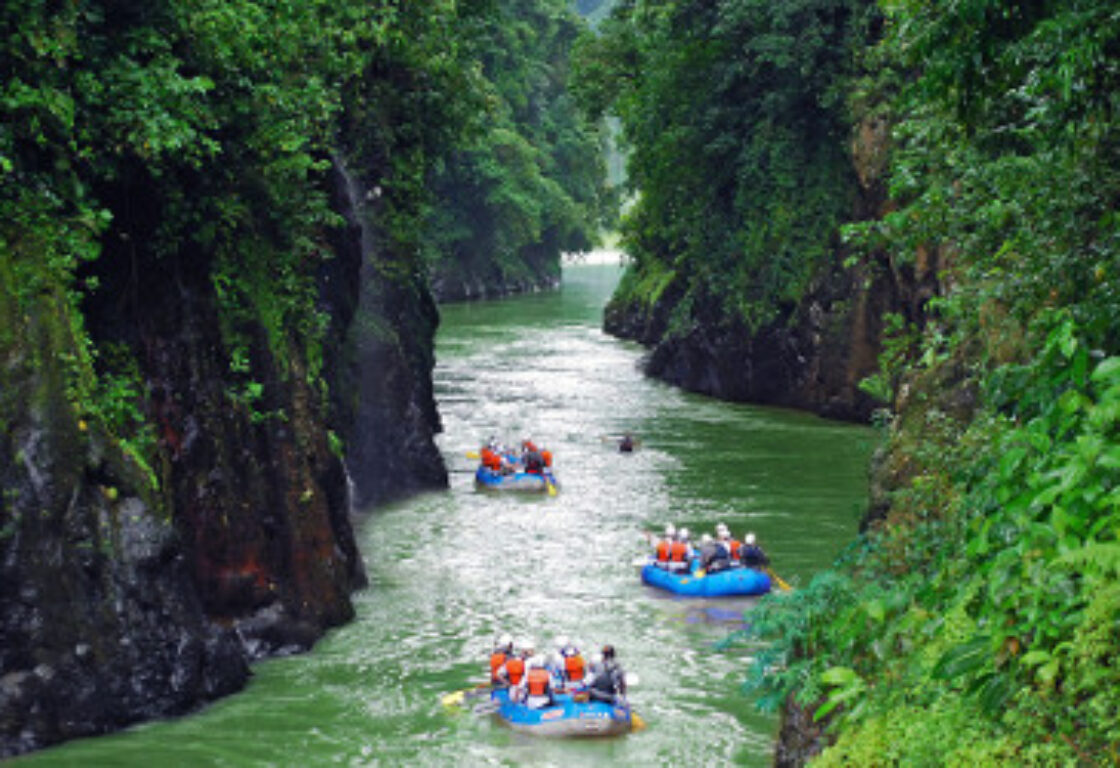 three blue rafts filled with people in red safety vests rafting on the river
