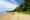 a distance shot from the beach of a beach bungalow hidden in the green trees but located directly on the beach by the ocean