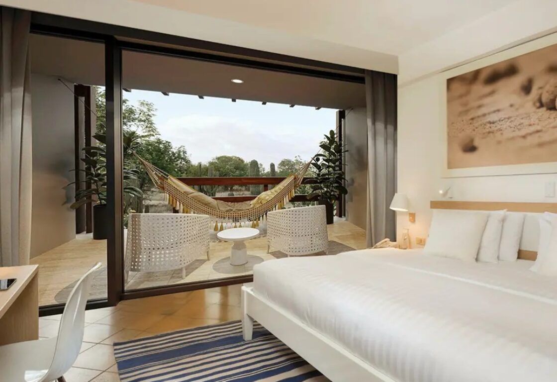 Finch Bay room with large white bed, blue and white striped rug, view onto the private terrace with a white hammock, comfy chairs overlooking the nature