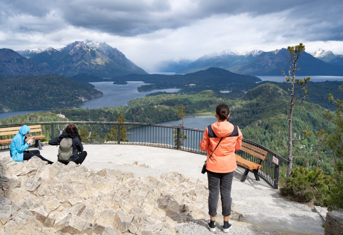 Tourists at the Viewpoint of Cerro Campanario, in Argentina's Lake District, showing Laguna El Trebol and Lago Perito Moreno below and a mountain range beyond