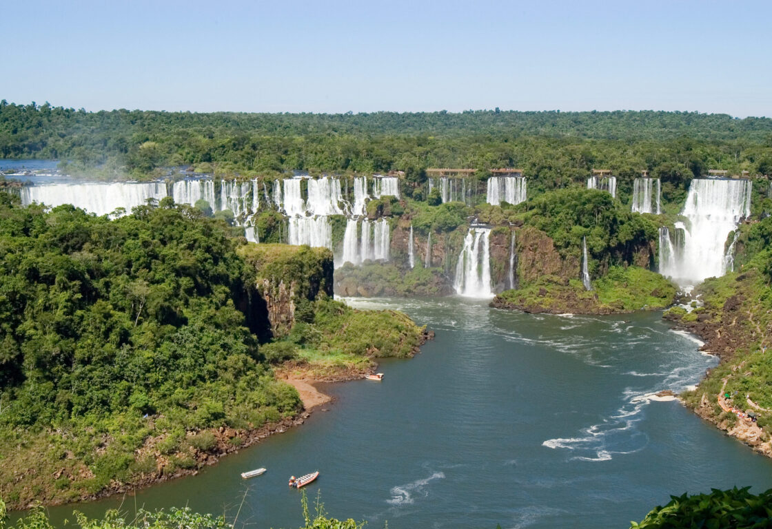 Iguazu Falls pictured from a high riverbank opposite, also showing boats arriving at San Martin Island