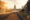 Sunset panoramic shot of a large period building with a tall spire in the middle, leading up to it is a gravel road with grass gardens on either side and a fountain in the middle.