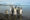 Around 15 Emperor penguins at the shore of a sea/lake with the view of cliffs in the distance