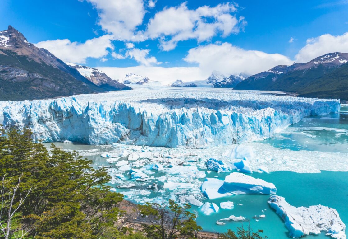 Aerial view of sprawling glacier. Snow capped mountains on either side of the glacier.