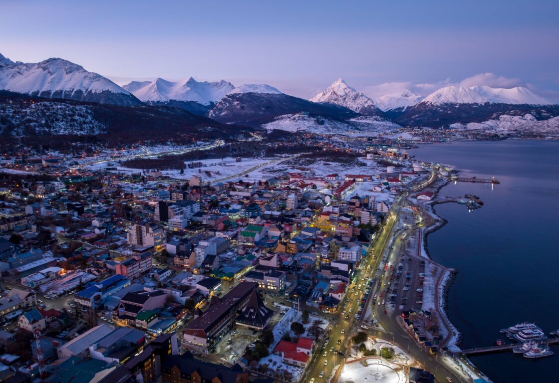 Sunset aerial shot of a small snowy town with a coastline and lots of snowy mountains