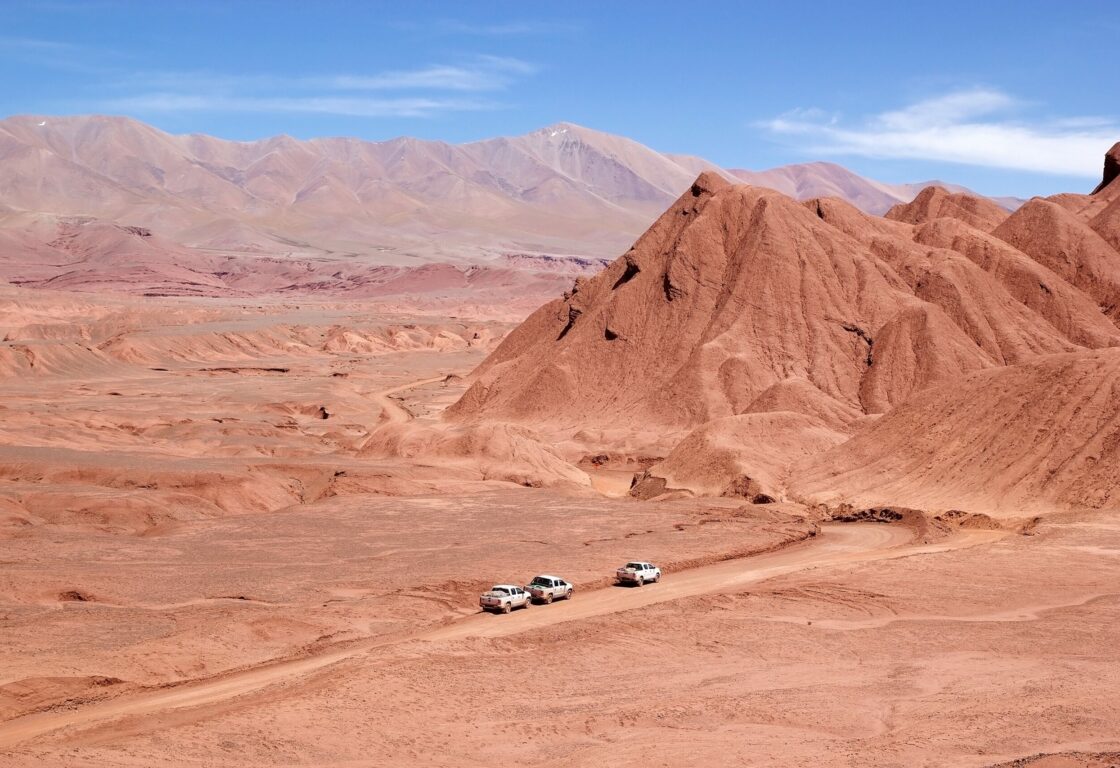 Aerial shot of cars driving through the surreal red landscape of the Desierto del Diablo, Northwest Argentina