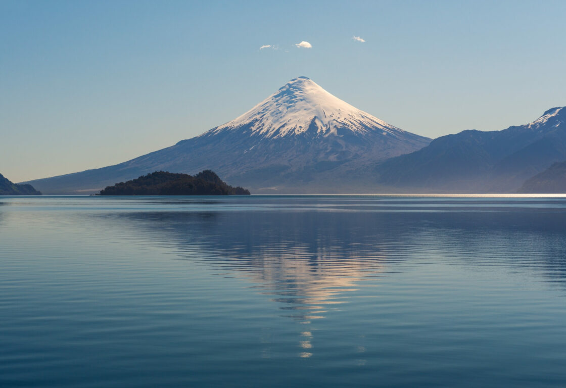 Cartoon-like picture perfect volcano with a snow covering its peak, in front of a peaceful lake
