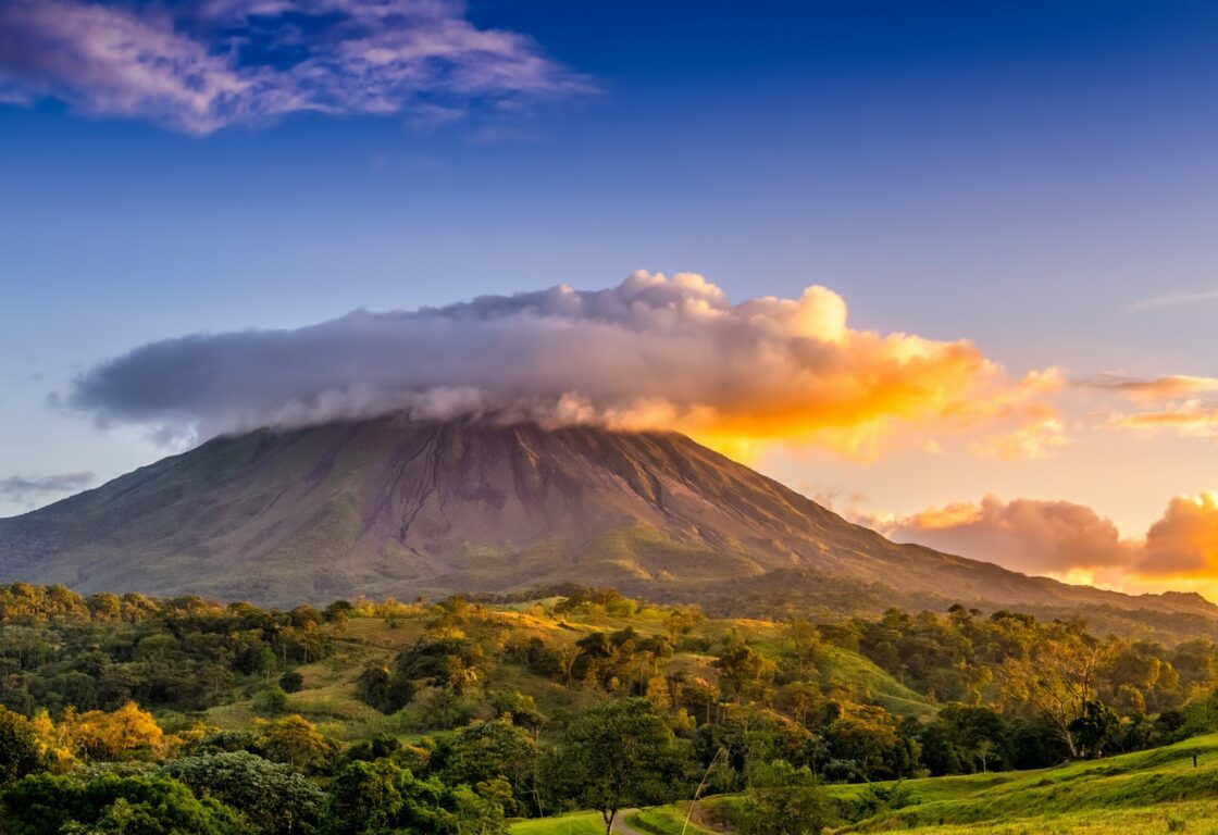A scenic view of a mountain surrounded by clouds and trees, showcasing a breathtaking landscape with the sky at sunset.
