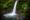 A woman stands at the bottom of a natural pool that a waterfall is flowing into. Area is surrounded by lush greenery