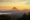 A triangular conical volcano breaks through the clouds at sunset