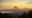 A triangular conical volcano breaks through the clouds at sunset