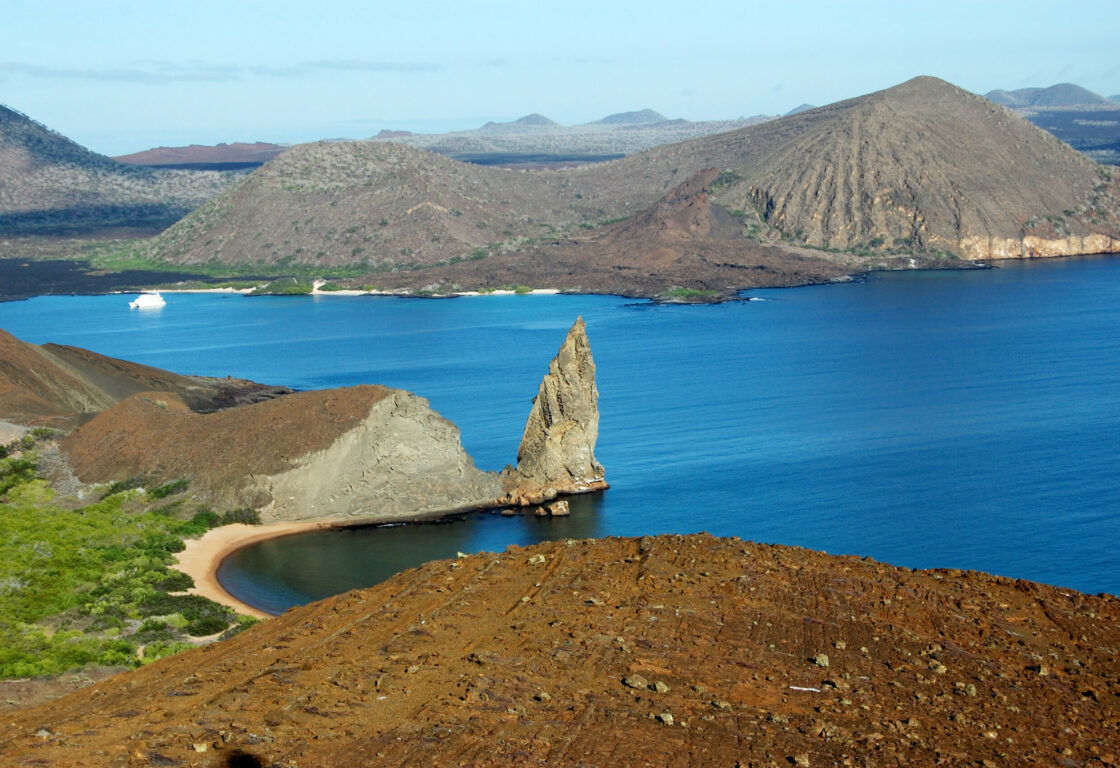 Taken from the summit of Bartolome Island, looking out at the rest of the island's volcanic structures, including pinnacle rock, a sharp, tall rock formation that juts out at the islands edge, looking out over the water.