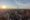 Aerial view of a city skyline at sunset, with tall buildings and a prominent tower under a partly cloudy sky, evoking a serene, golden ambiance.