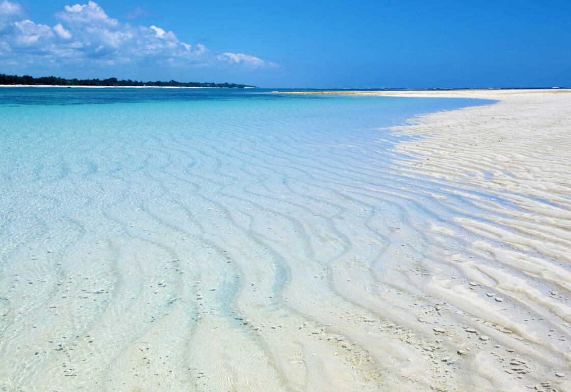 Closeup shot of sea shore with crystal clear blue water meeting wave rippled brilliant white sand