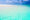 Clear turquoise ocean water gently meets a pristine white sandy beach under a bright blue sky with scattered clouds, evoking tranquility and serenity.