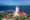 a white light house with a surrounding bulding with red roofes perched on the edge of the ocean