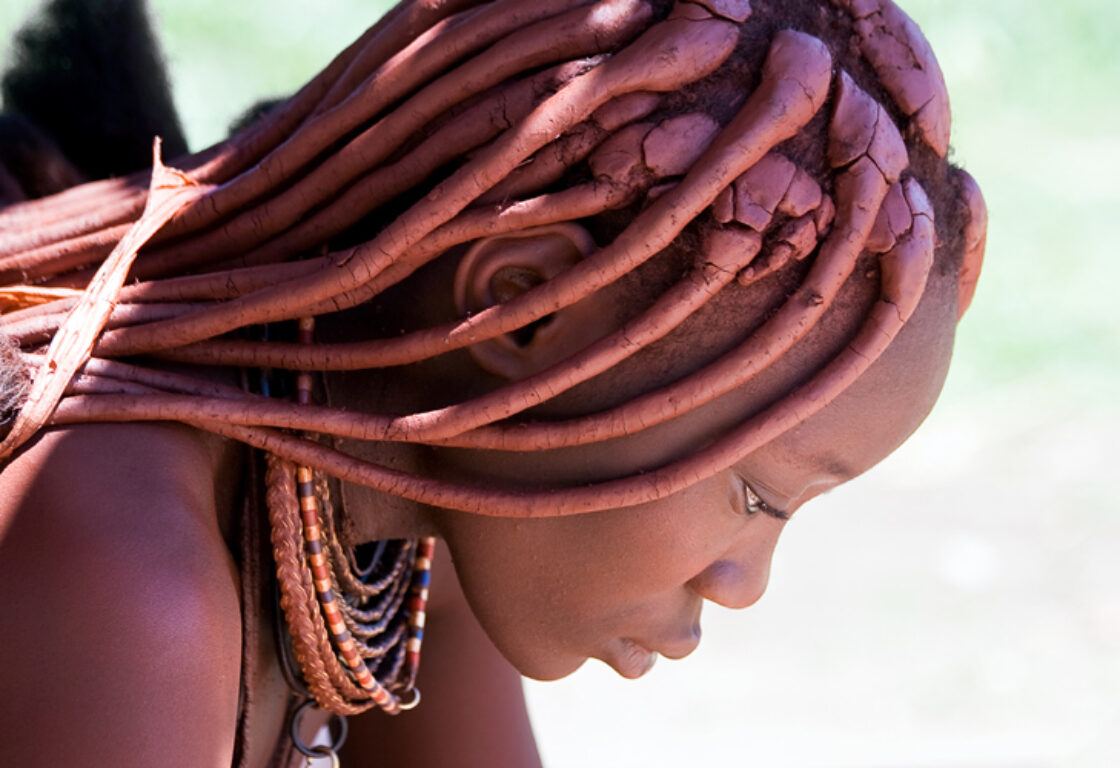a side profile photo of a himba woman from a traditional tribe in Namibia with hair plated, large neckalces