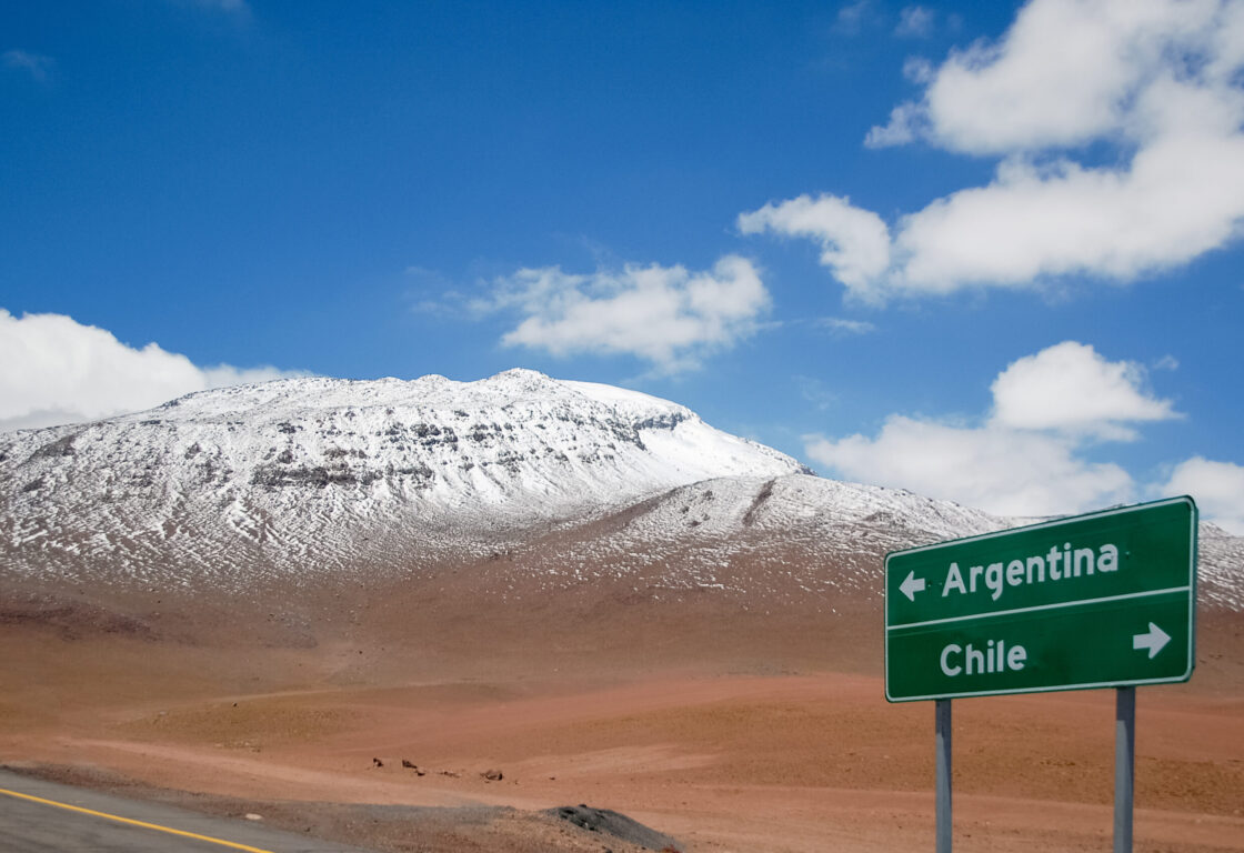 Highway sign with directions for Argentina and Chile at the border. Road sign in with mountain range and snow in the background.