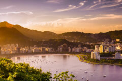 an aerial view of a Aterro do Flamengo bay at sunset featuring buildings, ocean and hills in the background, Rio de Janeiro, Brazil