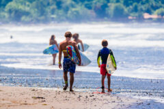 two boys in wetsuits walking towards the ocean holding their surf boards