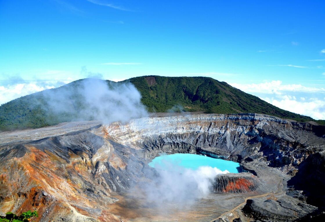 an aerial view of Poas Volcano crater with crystal blue water and a rock formation around it