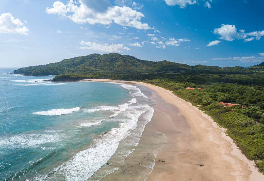 long stretch of Tamarindo beach fringed by green lush forest and palm trees