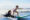 Little surf girl - young surfer learn to ride on surfboard with instructor at surfing school. Active family lifestyle, kids water sport lessons, swimming activity in summer camp. Vacation with child.