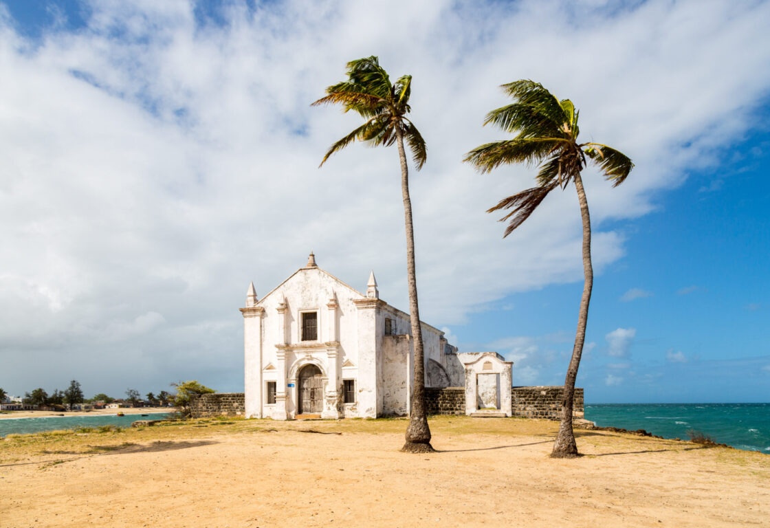 Church and fortress of San Antonio on Mozambique island, with two palm trees on sand. Indian ocean coast, Nampula province, Mozambique. Fortim de Santo António na Ilha de Moçambique.
