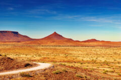 a landscape view of a dirt road through the vast savanah and rock formations in Damaraland Namibia